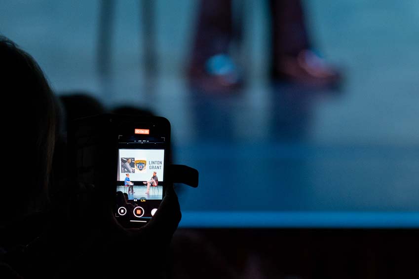 A photo of someone filming an interview with Linton Grant on their phone