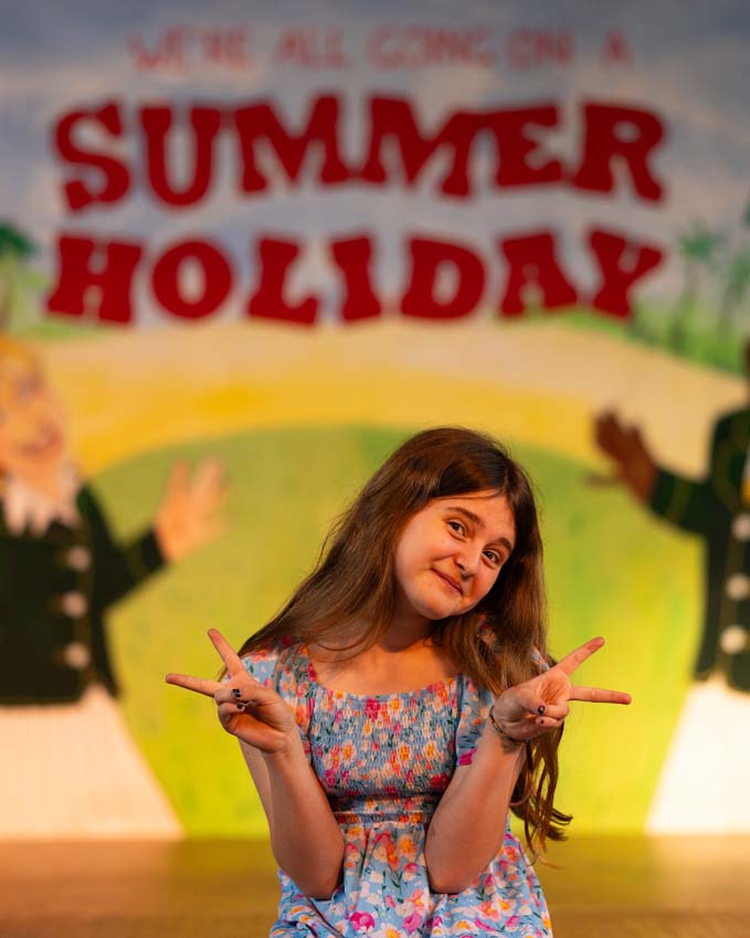 Cast member sat on stage for We're all going on a summer holiday at Poplins primary school performance amazing set painted by Sally Renner Normanton Rutland