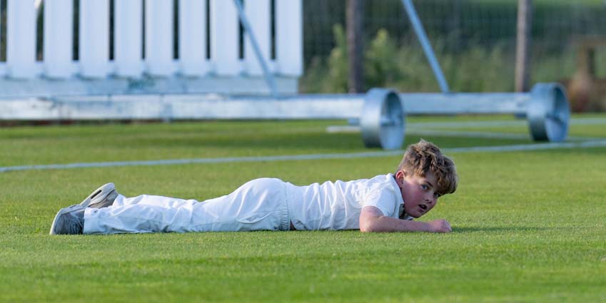 Junior cricket player laying on ground fielding