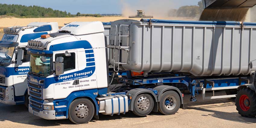 Coopers Transport Essex having two trucks loaded with grain in Northamptonshire with Conant Farming combining in the background