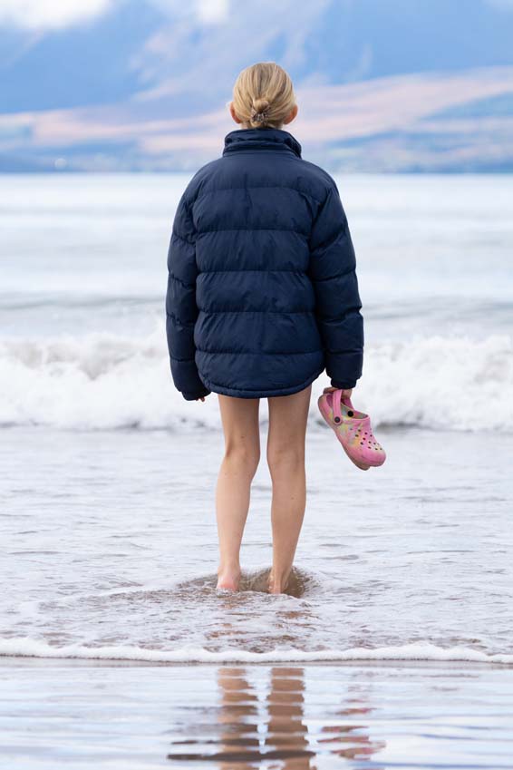 Teenage girl standing on the shoreline looking out to sea